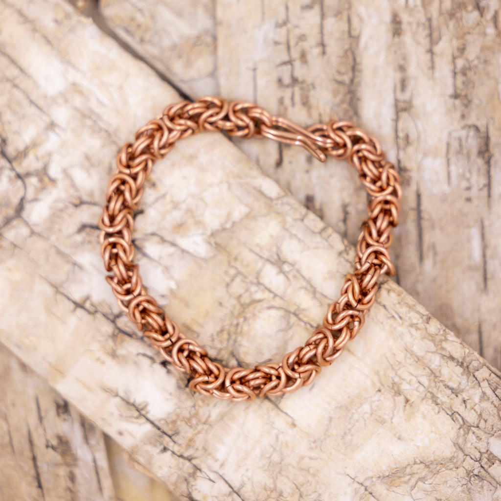 Image shows a bracelet of interlocking copper rings on a pale wood background.