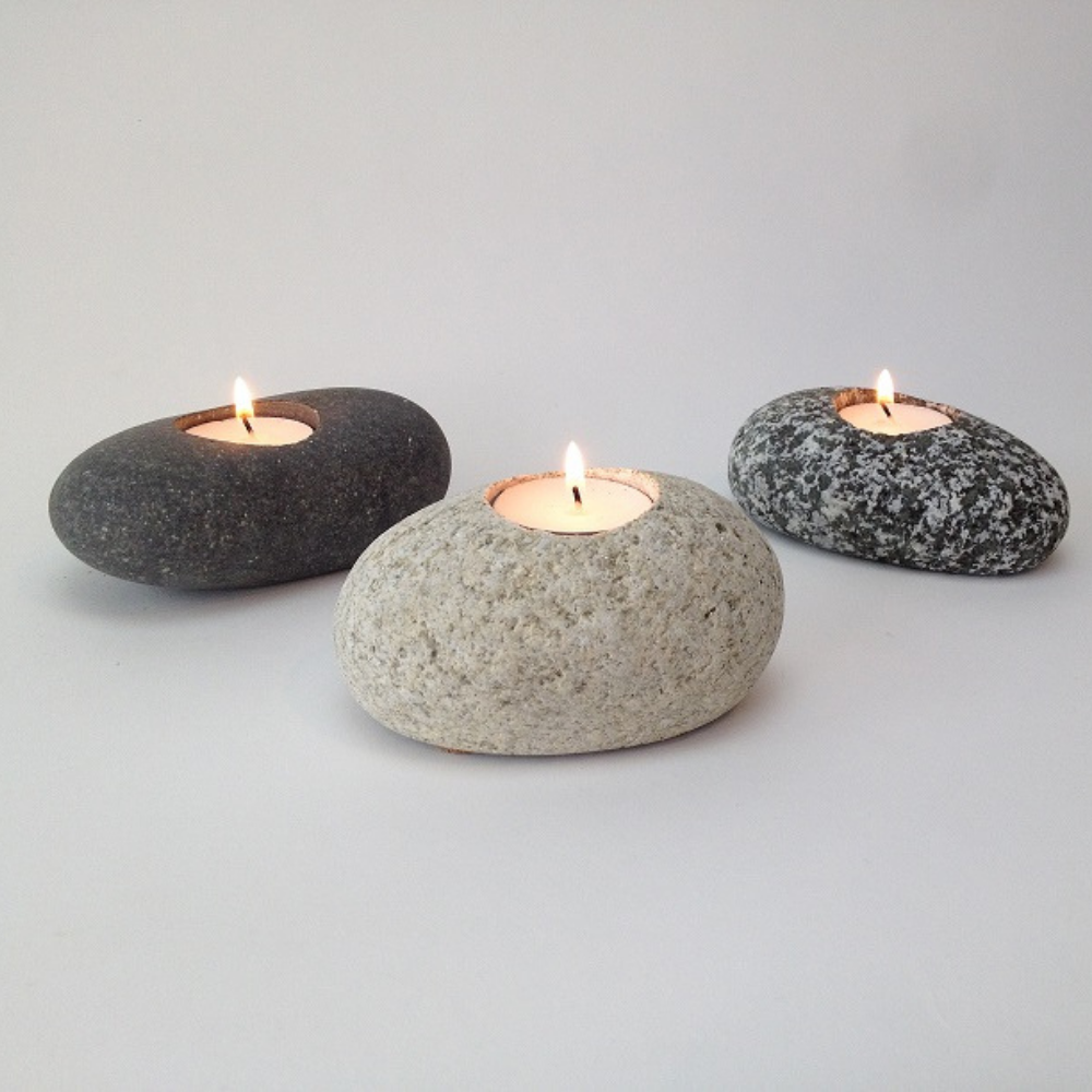 Image shows three tea lights in natural river stone holders on a nondescript gray background