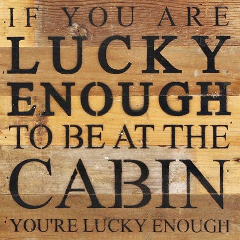 Image shows a natural wood sign. Text reads "If you are lucky enough to be at the cabin, you're lucky enough."