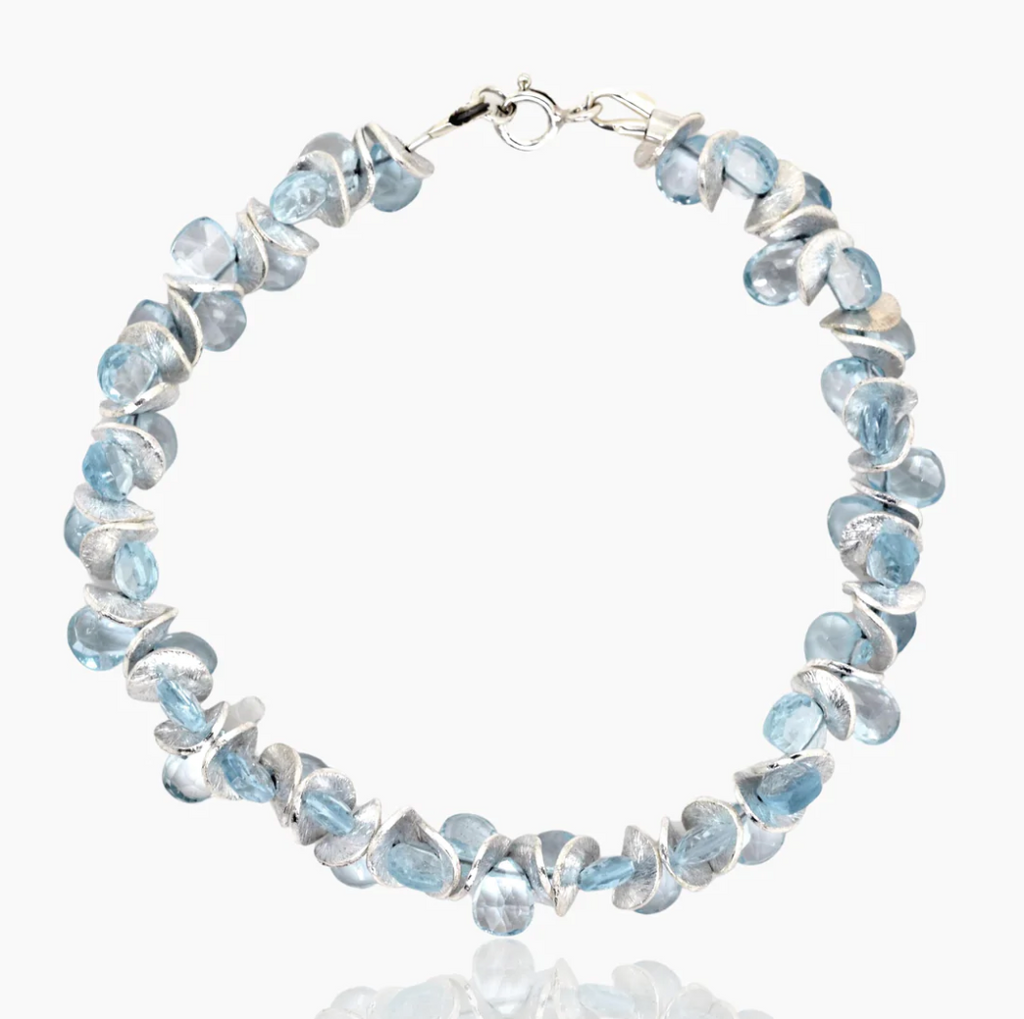 Image shows a bracelet of translucent translucent blue topaz beads alternating with sterling silver discs on a white background.