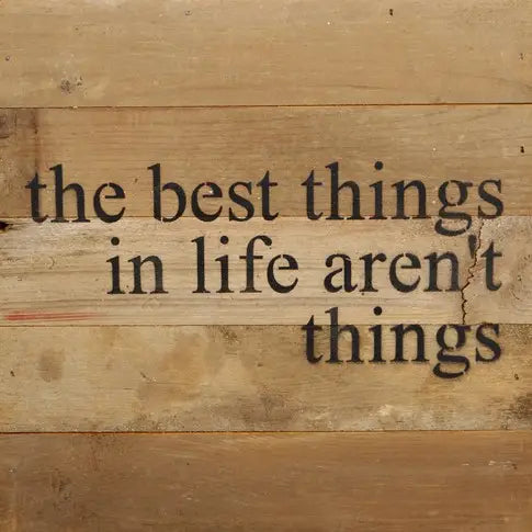 Image shows a natural wood sign. Text reads "The best things in life aren't things".