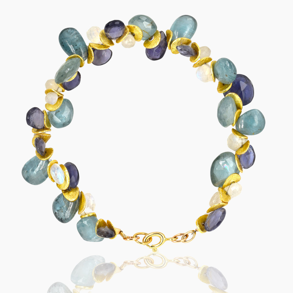 Image shows a bracelet with stones in various shades of blue and purple alternating with gold discs on a white background.