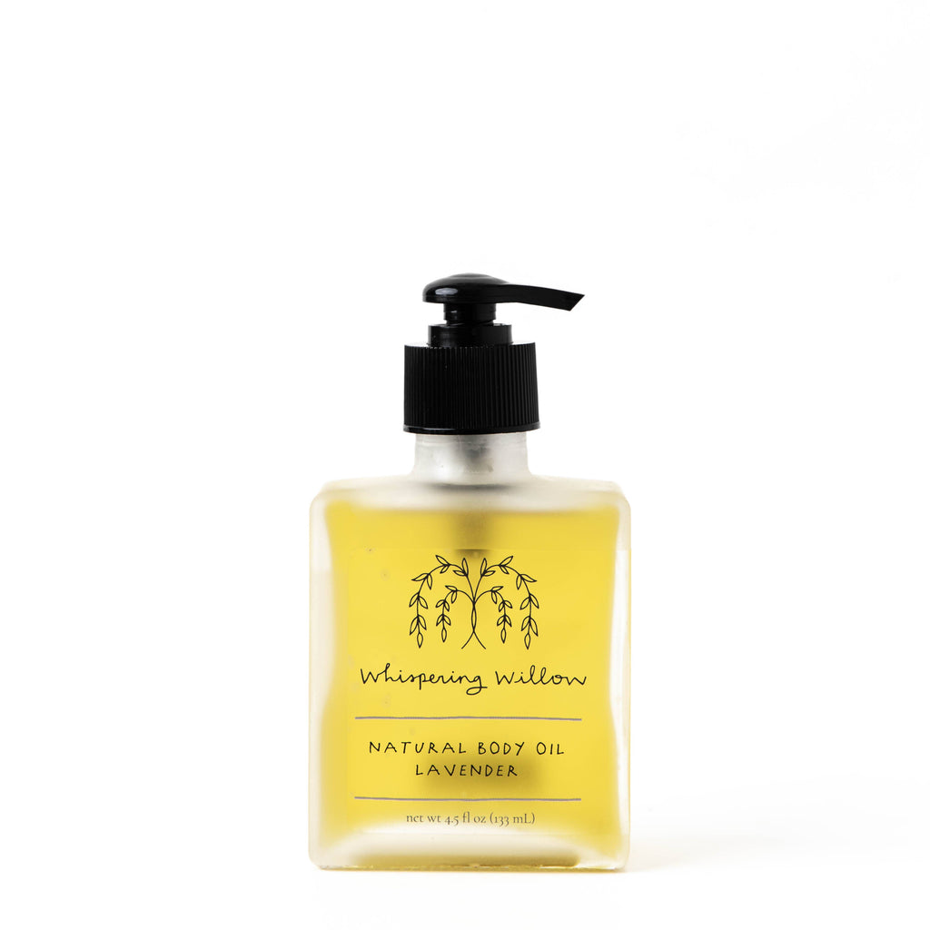 Image shows a clear, square bottle of yellow body oil on a white background.